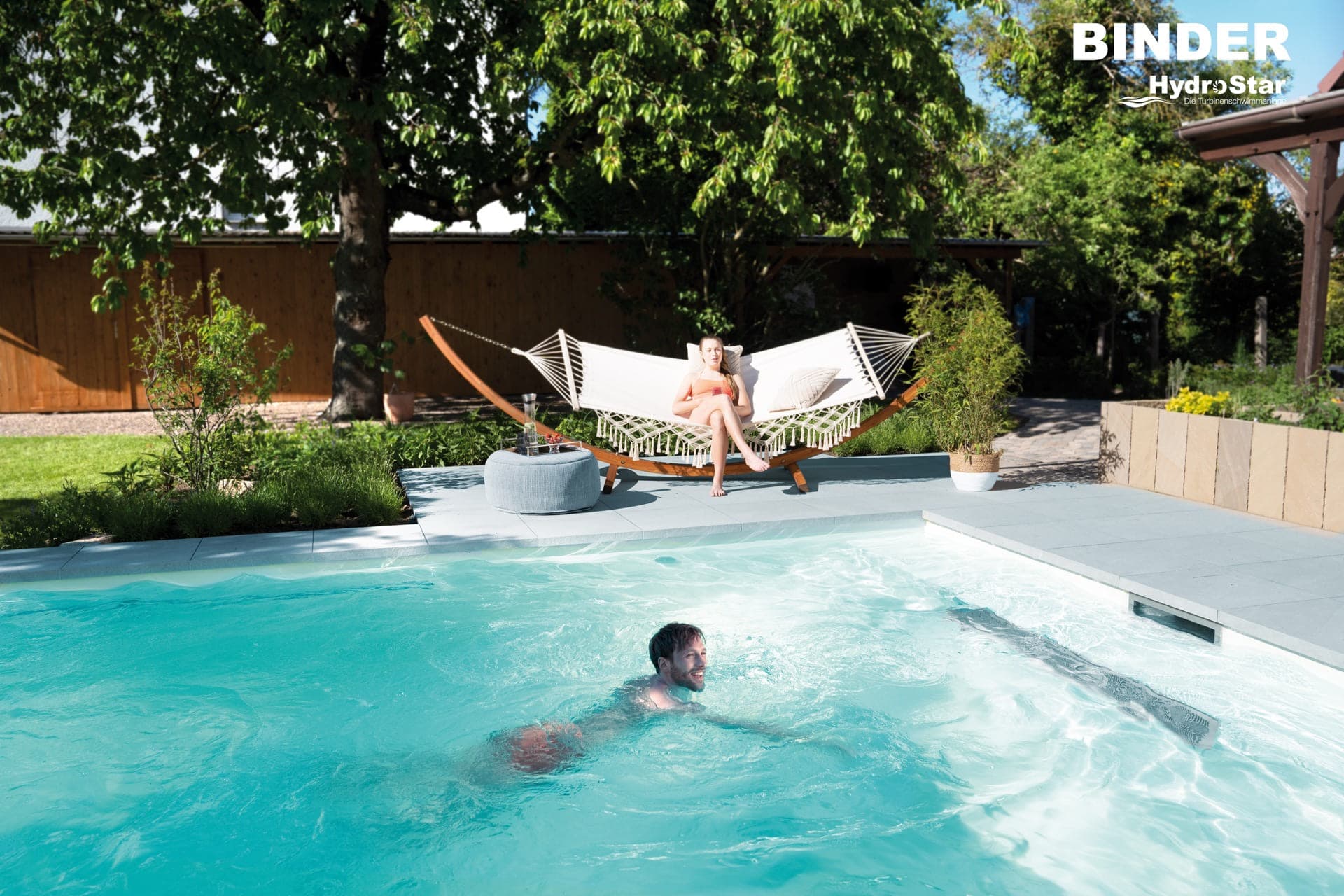 Man swimming in a private garden pool while a woman relaxes in a hammock beside the terrace, surrounded by lush greenery and mature trees