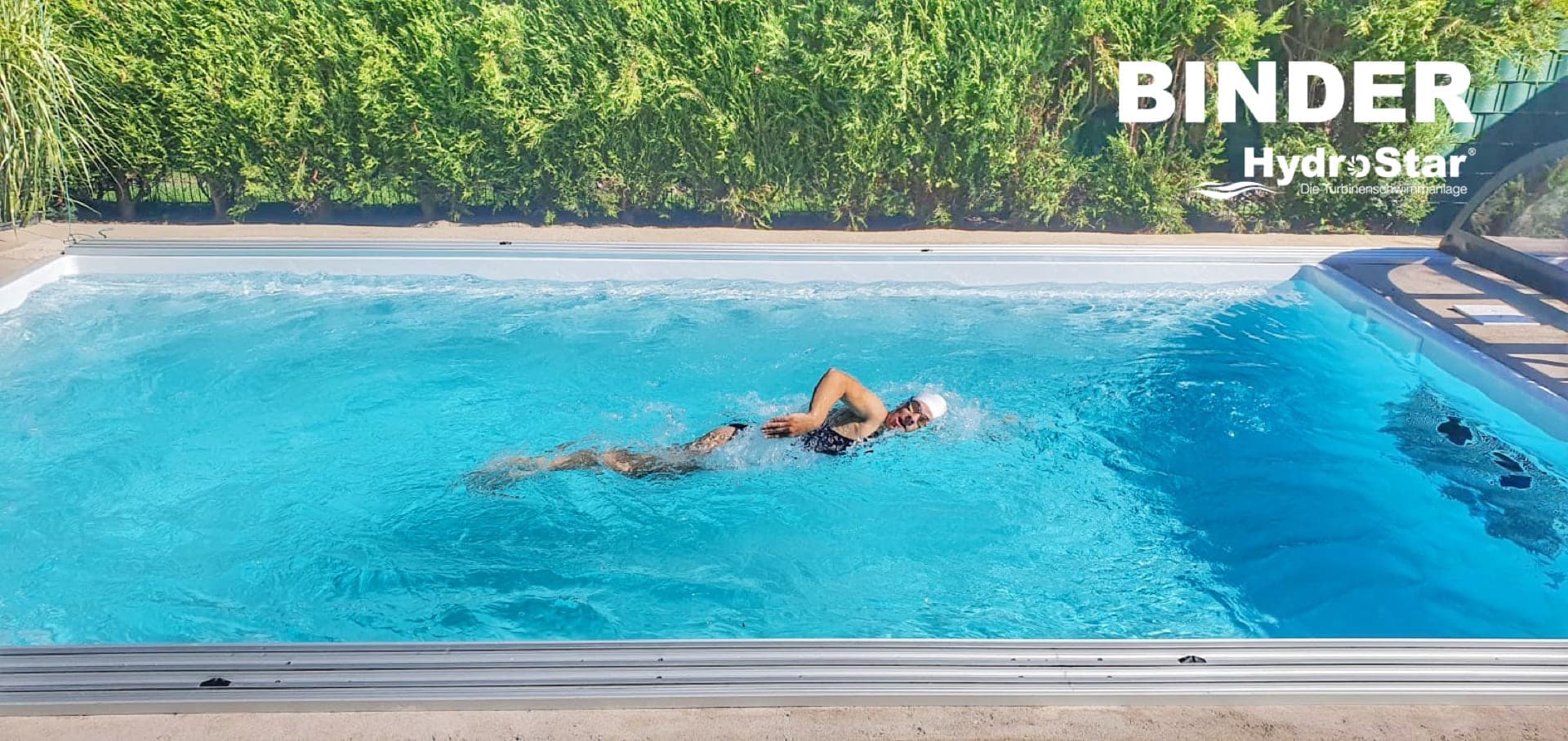 Swimmer doing freestyle in an outdoor pool with lush green surroundings, viewed from above